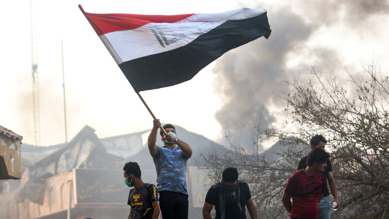 1028575176 An Iraqi protester waves a national flag while demonstrating outside the burnt-down local government headquarters in the southern city of Basra on September 7, 2018 during demonstrations over poor public services. - Basra has seen a surge in protests since September 4, with demonstrators torching government buildings as well as political party and militia offices, as anger boils over after the hospitalisation of 30,000 people who had drunk polluted water. (Photo by Haidar MOHAMMED ALI / AFP) (Photo c
