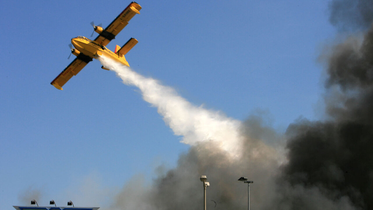 TURKEY AIRPORT FIRE A firefighter plane douses water over the black smoke and flames raging through the cargo section at Ataturk International Airport in Istanbul May 24, 2006. REUTERS/Fatih Saribas - GM1DSRFSRLAA