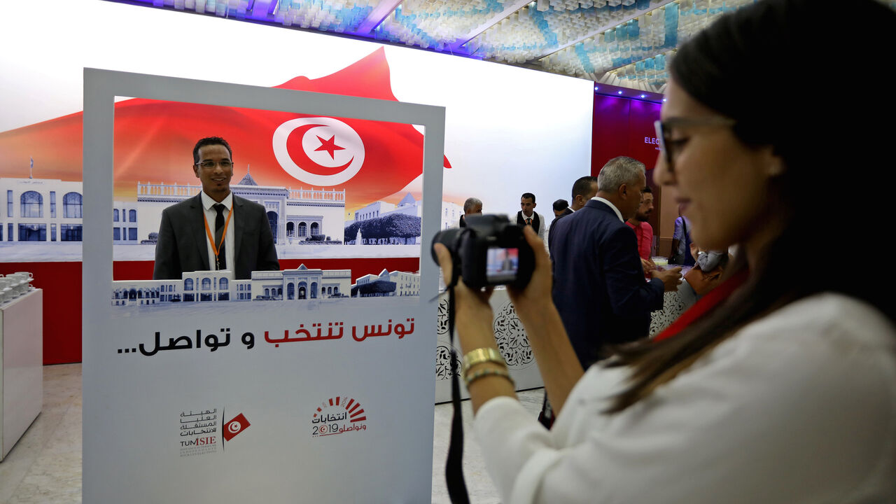 TUNISIA-ELECTION/ A man poses for a picture with a poster that reads in Arabic "Tunis, Elect and Continue" during the opening of the media center for the presidential election in Tunis, Tunisia, September 12, 2019. REUTERS/Muhammad Hamed - RC1110D7B900