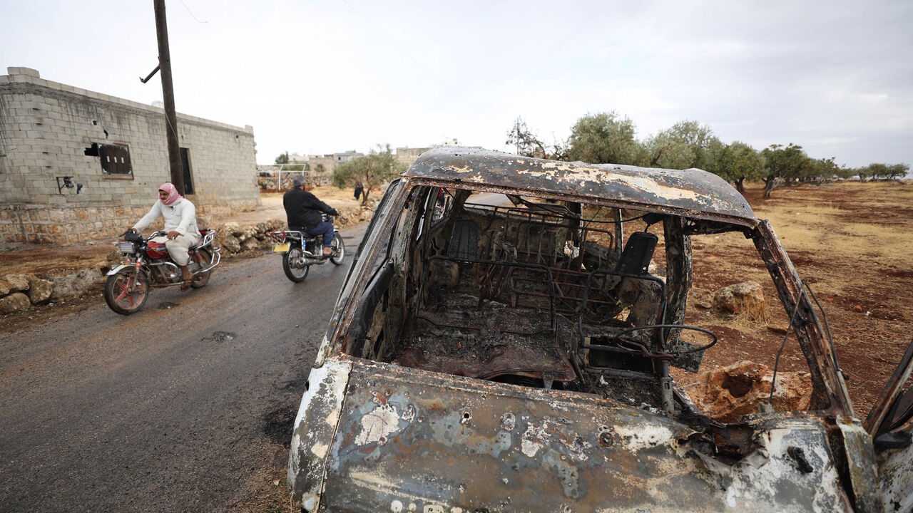 1178650382 A picture taken on October 28, 2019 shows Syrian bikers riding past a damaged car at the site of a suspected US-led operation against Islamic State (IS) chief Abu Bakr al-Baghdadi the previous day, on the edge of the small Syrian village of Barisha in the country's opposition-held northwestern Idlib province. - US President Donald Trump announced that Baghdadi, the elusive leader of the jihadist group and the world's most wanted man, was killed in the early hours of Octobe 27 in an overnight US raid near th