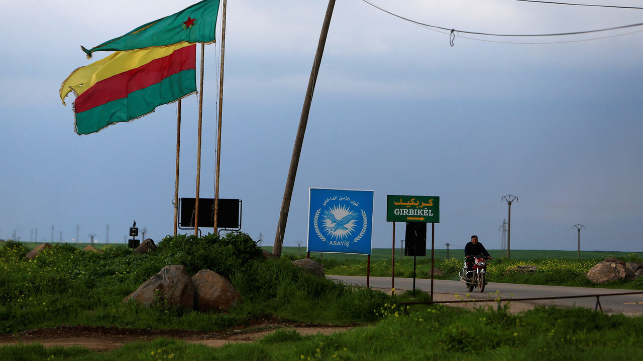SYRIA-ISLAMIC STATE/ A man rides on a motorbike past a Kurdish female fighters of the Women's Protection Unit (YPJ) flag in the town of Rmeilan, Hasaka province, Syria March 28, 2019. Picture taken March 28, 2019. REUTERS/Ali Hashisho - RC1B20B29D90