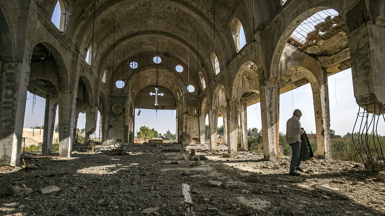 1183277571 Sarkoun Selio, a 50-year-old Assyrian Christian Syrian and one of the few Assyrians still living there, walks in the ruins of the Assyrian Church of the Virgin Mary, which was previously destroyed by Islamic State (IS) group fighters, in the village of Tal Nasri south of the town of Tal Tamr in Syria's northeastern Hasakah province on November 15, 2019. - The few Assyrian Christians who escaped the Islamic State group invasion in 2015, and did not choose to emigrate, now anxiously watch the advance of Turki