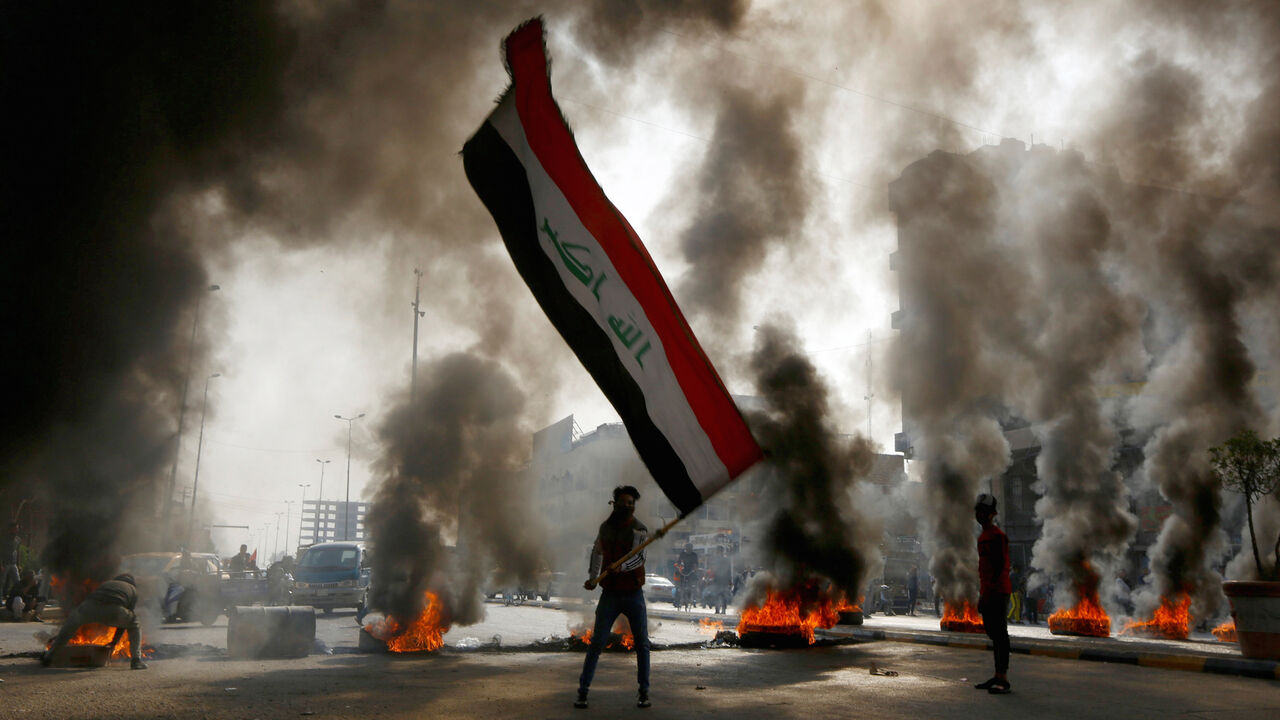 IRAQ-PROTESTS/ A protester holds an Iraqi flag amid a cloud of smoke from burning tires during ongoing anti-government protests in Najaf, Iraq November 26, 2019. REUTERS/Alaa al-Marjani - RC2ZID9MARY6