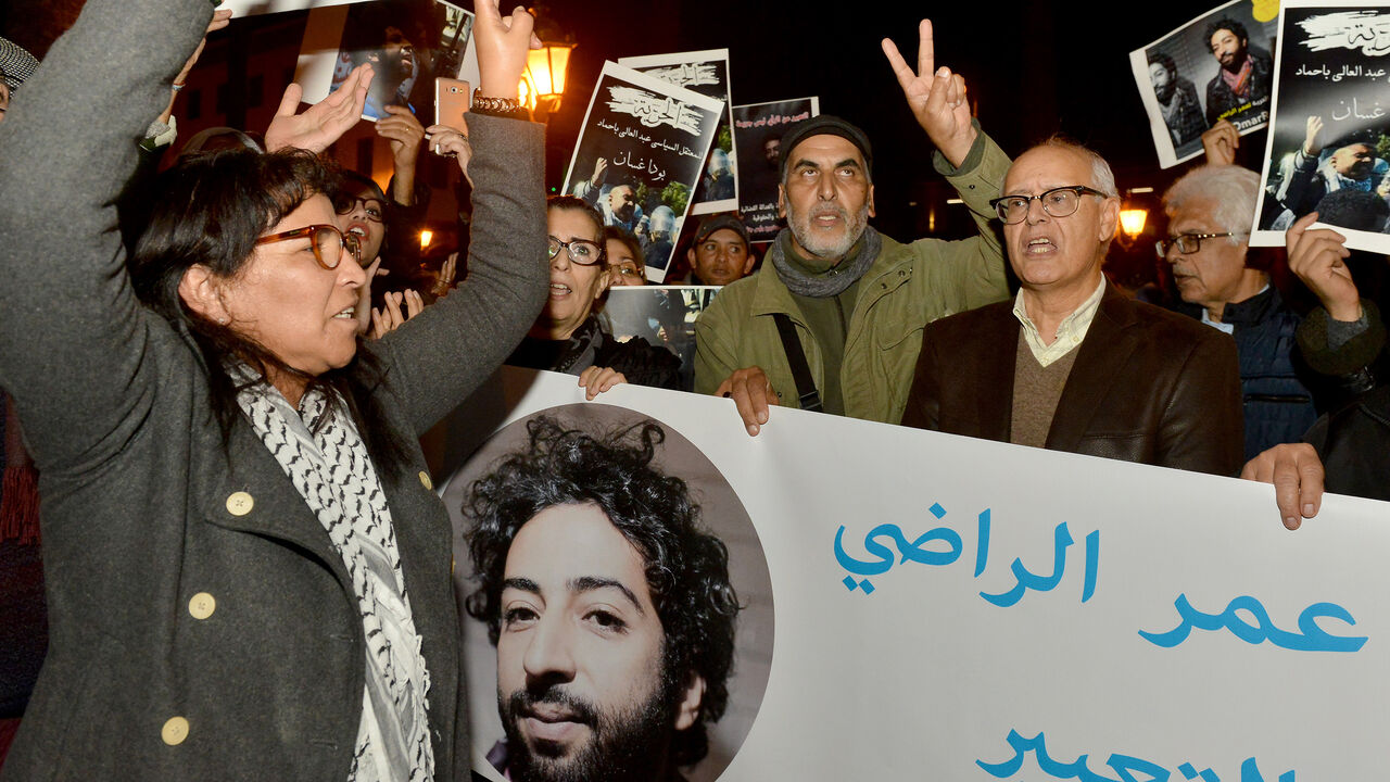 1190703460 Demonstrators shoot slogans and hold a banner showing a portrait of Omar Radi, a Moroccan journalist detained over tweet criticising judge, during a demonstration, on December 28, 2019, in the city of Rabat. (Photo by STR / AFP) (Photo by STR/AFP via Getty Images)