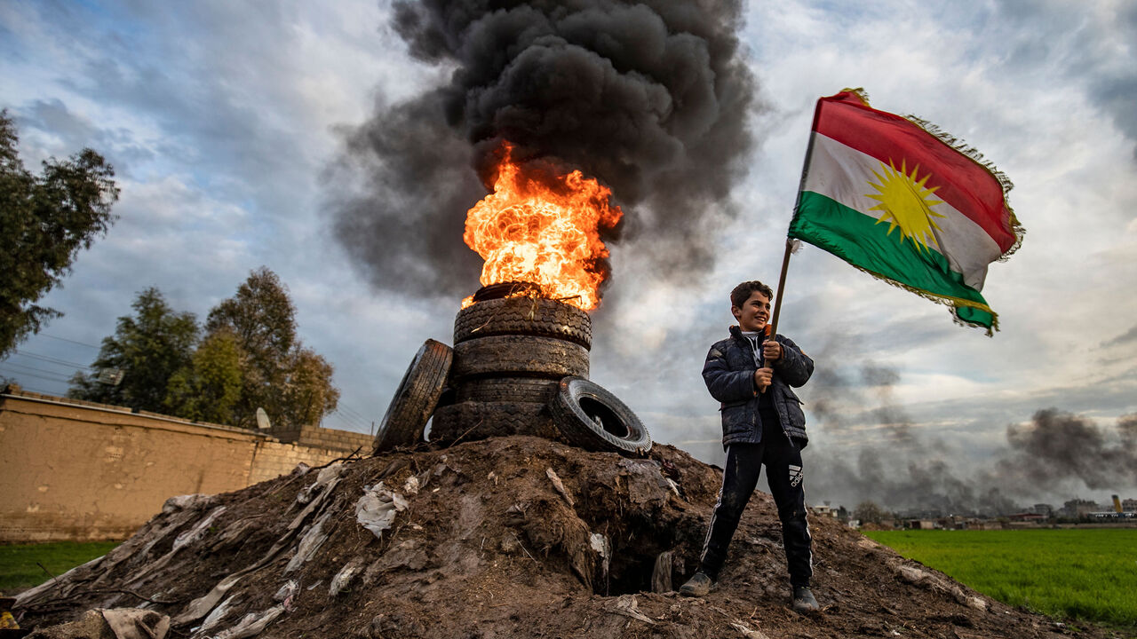 1207850125 A boy stands holding a Kurdish flag near a bonfire marking the Kurdish holiday of Noruz in Qamishli in Syria's northeastern Hasakah province on March 20, 2020, after the local authorities cancelled holiday celebrations due to fears of the spread of COVID-19 coronavirus disease. - The Persian New Year is an ancient Zoroastrian tradition celebrated by Iranians and Kurds which coincides with the vernal (spring) equinox and is calculated by the solar calendar. (Photo by DELIL SOULEIMAN / AFP) (Photo by DELIL SO