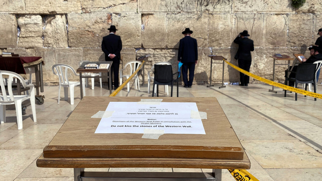 HEALTH-CORONAVIRUS/JERUSALEM-JUDAISM Ultra-Orthodox Jewish men pray in front of the Western Wall, Judaism's holiest prayer site, in Jerusalem's Old City as a note advice not to kiss the stones of the Western Wall display March 16, 2020 REUTERS/ Ilan Rosenberg - RC21LF90G2FL