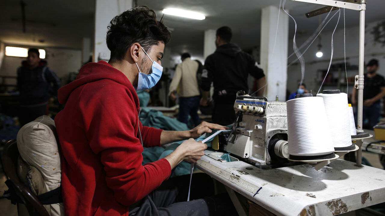 1208743602 A palestinian worker manufacture protective coverall suits and masks at a workshop in Gaza City on March 31, 2020. amid coronavirus COVID-19 pandemic. Factories in the Gaza Strip used to specialize in the manufacture of shirts and jeans, for despite the closure of many of them in previous years due to the blockade imposed on the Gaza Strip and the inability to export and its aftermath From economic problems that led to the closure of many factories, But with the invasion of the new coronavirus to the world,