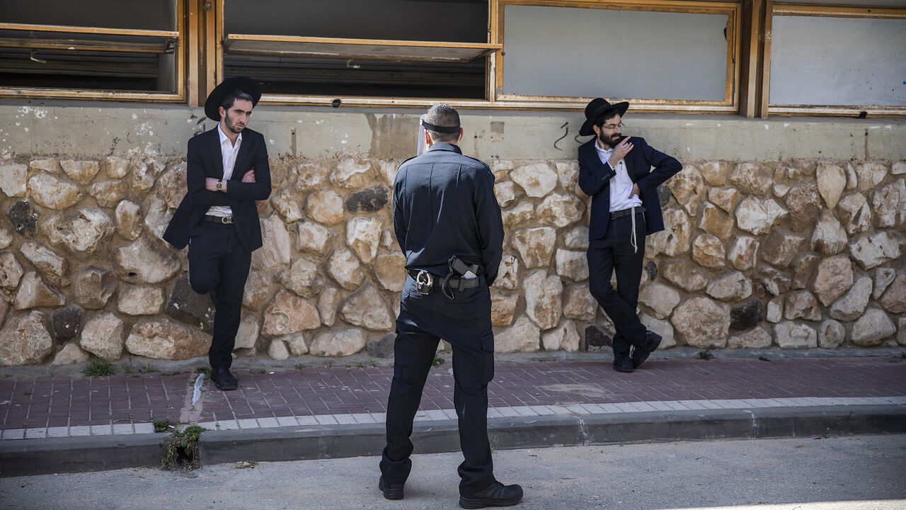 1208944142 02 April 2020, Israel, Bnei Brak: An Israeli policeman stops Orthodox Jews, who insist on carrying on with their prayer at the Ponevezh Yeshiva, a Jewish institution that focuses on the study of traditional religious texts, despite the imposed lockdown amid the coronavirus pandemic. Photo: Ilia Yefimovich/dpa (Photo by Ilia Yefimovich/picture alliance via Getty Images)