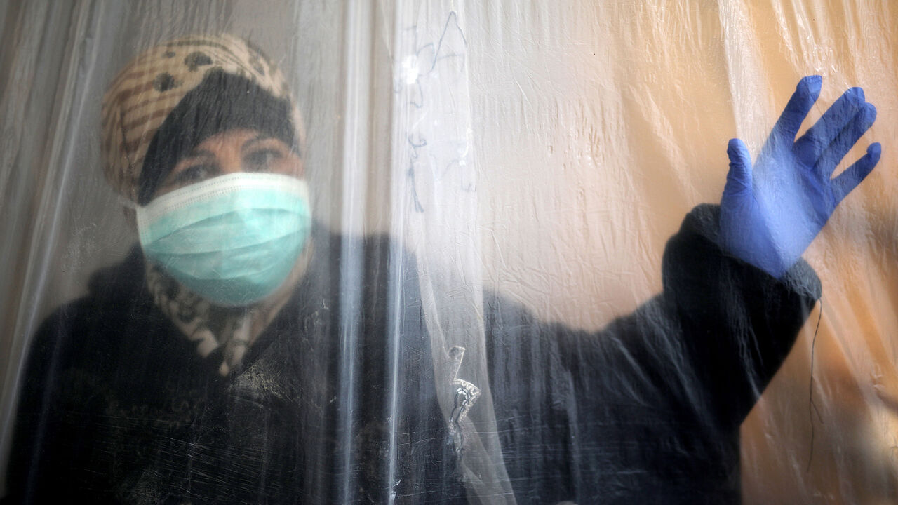 1209676569 A woman wearing a protective mask and glove looks out through a nylon sheet covering part of she house in Beit Lahiya, northern Gaza Strip during the novel coronavirus pandemic crisis,on 11 April 2020. (Photo by Majdi Fathi/NurPhoto via Getty Images)