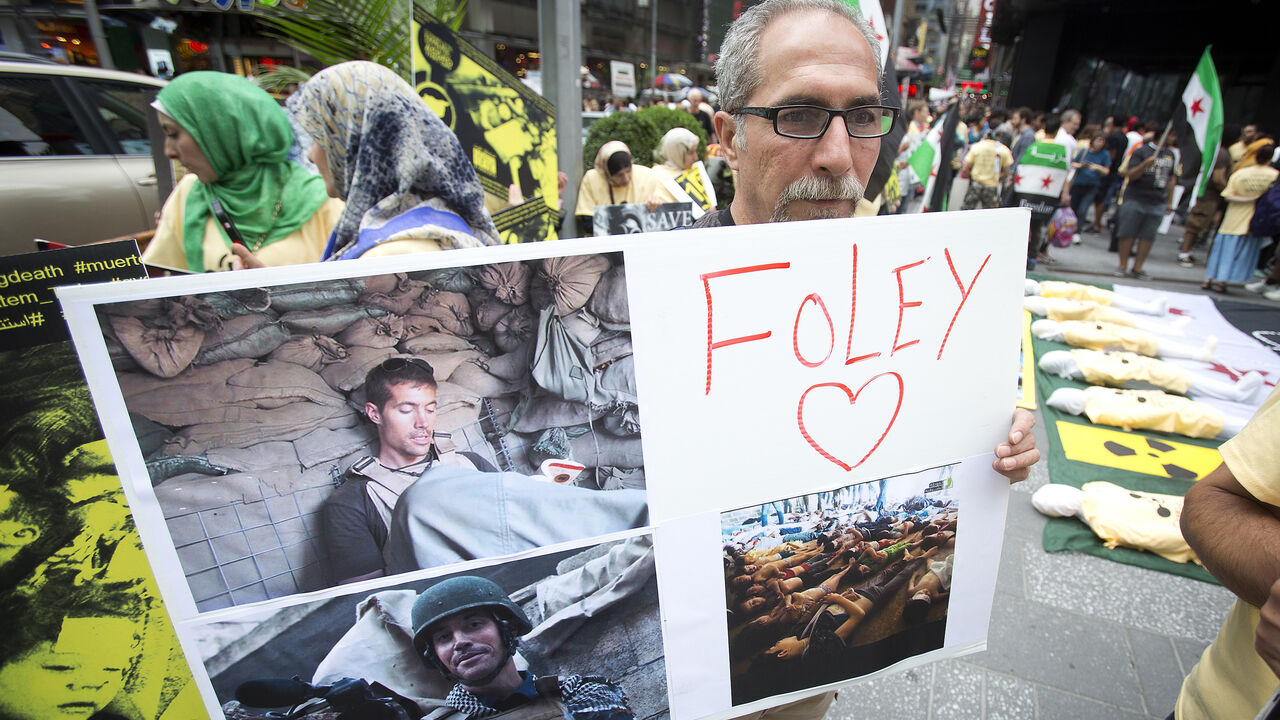 USA-PROTEST/ A man holds up a sign in memory of U.S. journalist James Foley during a protest against the Assad regime in Syria in Times Square in New York August 22, 2014. Foley, who was abducted in Syria in late 2012, was beheaded by a masked member of the Islamic State group in an act filmed in a video released on August 19 that also threatened a second American journalist, Steven Sotloff. REUTERS/Carlo Allegri (UNITED STATES - Tags: SOCIETY CIVIL UNREST) - GM1EA8N0MAY01