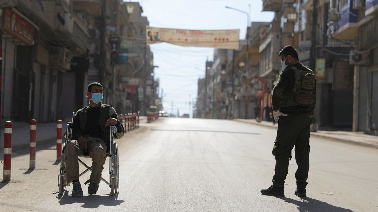 HEALTH-CORONAVIRUS/SYRIA A member of the Asayish stands near a man in a wheelchair along an empty street, as restrictions are imposed as measure to prevent the spread of the coronavirus disease (COVID-19) in Qamishli, Syria March 23, 2020. REUTERS/Rodi Said - RC2VPF9ALD0J