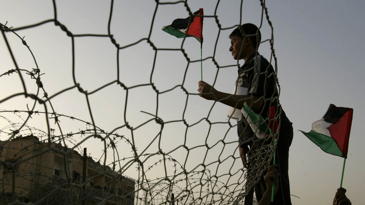 PALESTINIANS-ISRAEL/ A Palestinian waves the national flag as he stands near the border wall between Egypt and the Gaza Strip, during a protest calling for an end of Israel blockade to the Gaza Strip, April 10, 2008. . REUTERS/Ibraheem Abu Mustafa (GAZA) - GM1E44B08HW02
