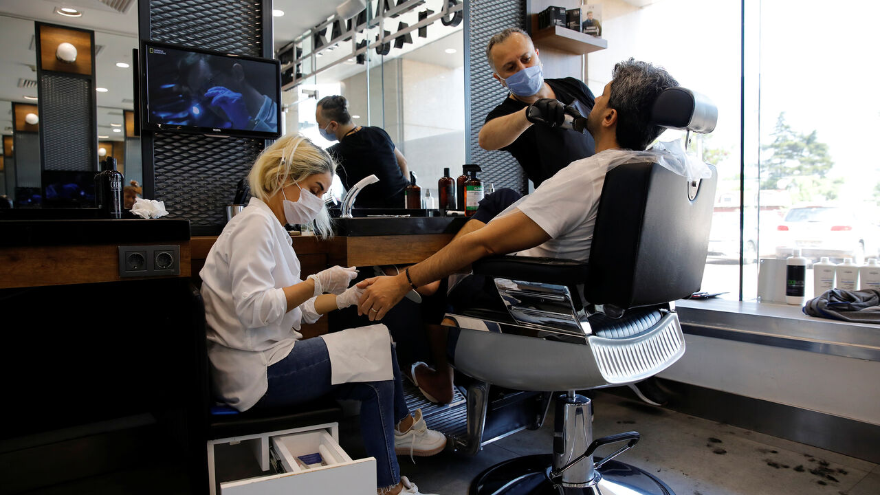 An employee trims beard of a client as the other one gives him manicure, on the first day of the reopening of a hair salon which was closed since March 21 amid the spread of the coronavirus disease (COVID-19), in Istanbul, Turkey, May 11, 2020. REUTERS/Umit Bektas - RC2BMG9ZPB5E