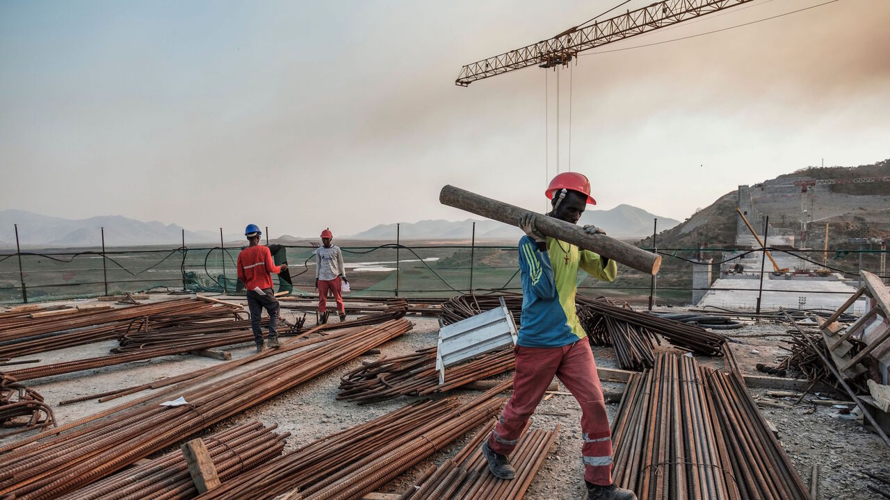 1192325453 A worker walks with a piece of wood on his shoulder at the Grand Ethiopian Renaissance Dam (GERD), near Guba in Ethiopia, on December 26, 2019. - The Grand Ethiopian Renaissance Dam, a 145-metre-high, 1.8-kilometre-long concrete colossus is set to become the largest hydropower plant in Africa.
Across Ethiopia, poor farmers and rich businessmen alike eagerly await the more than 6,000 megawatts of electricity officials say it will ultimately provide.
Yet as thousands of workers toil day and night to finish