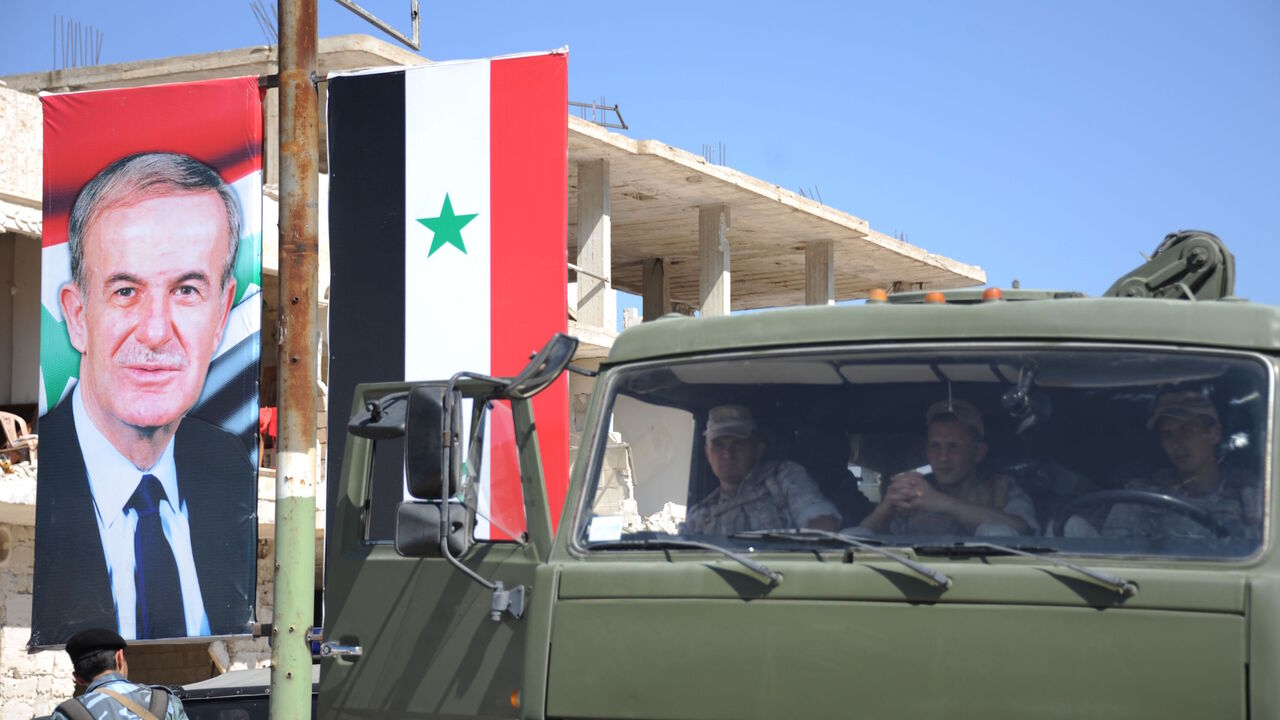 1171055173 Russian soldiers sit in their vehicle next to a portrait of late Syrian president Hafez al-Assad in Khan Sheikhun in the southern countryside of the Idlib province on September 25, 2019. - With military backing from Russia, President Bashar al-Assad's forces have retaken large parts of Syria from rebels and jihadists since 2015, and now control around 60 percent of the country. Russia often refers to troops it deployed in Syria as military "advisers" even though its forces and warplanes are also directly in