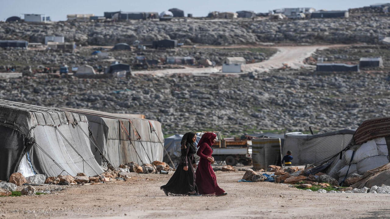 1206599399 TOPSHOT - Displaced Syrian women walk at a camp in Kafr Lusin village on the border with Turkey in Syria's northwestern province of Idlib, on March 10, 2020. - When protesters in March 2011 demanded their rights and regime change, they likely never imagined it would trigger a reaction that has led to the 21st century's biggest war. Nine years on, President Bashar al-Assad is still in power and there to stay, more than 380,000 people have died, dozens of towns and cities razed to the ground and half of the c