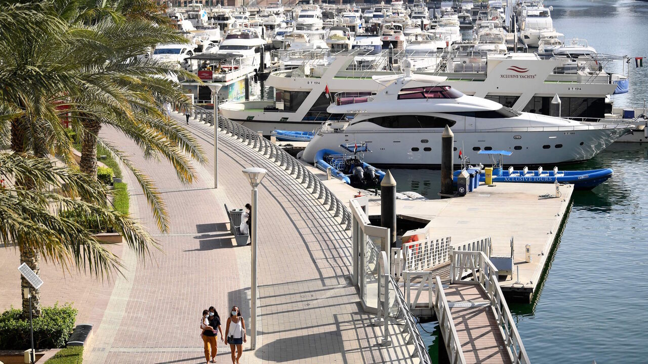 1212005086 Women wearing protective masks walk at the promenade of Dubai Marina on May 5, 2020, after authorities of the United Arab Emirates started to ease a national lockdown put in place to curb the spread of COVID-19 coronavirus. - In Dubai's ritzy Marina district, white yachts are tethered to docks, standing idle -- like many companies behind a luxury lifestyle industry battered by the coronavirus crisis. The boardwalks that snake around the precinct's artificial bays and canals, once packed with tourists, mostl