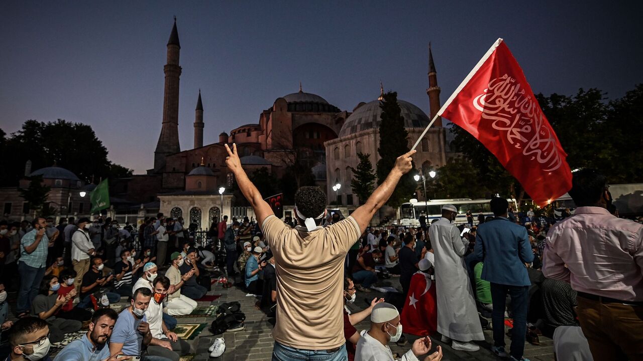 1226034187 A man flashes the V for Victory hand sign and waves a flag outside the Hagia Sophia museum in Istanbul on July 10, 2020 as people gather to celebrate after a top Turkish court revoked the sixth-century Hagia Sophia's status as a museum, clearing the way for it to be turned back into a mosque. - The Council of State, the country's highest administrative court which on July 2 debated a case brought by a Turkish NGO, cancelled a 1934 cabinet decision and ruled the UNESCO World Heritage site would be reopened t