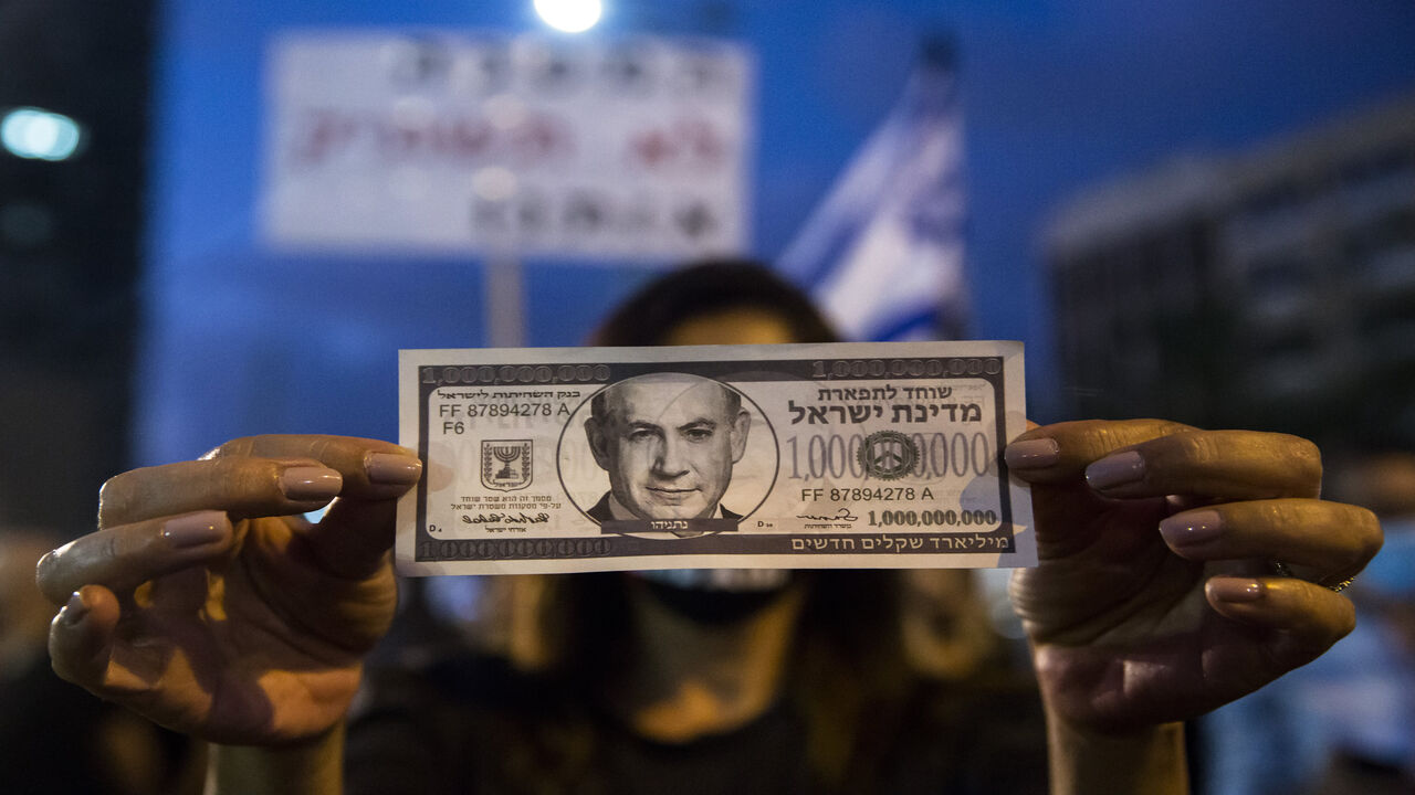 1226305353 TEL AVIV, ISRAEL - JULY 11: Israeli Protester holds a fake bill with a photo of the Israeli Prime Minister Benjamin Netanyahu as she protests against the Government's economy response to the cororna virus crisis on July 11, 2020 in Tel Aviv, Israel. Following a rise in the cases of COVID-19, Israeli Prime Minister Benjamin Netanyahu has ordered many businesses to shut, causing people to protest about a perceived mishandling of the coronavirus pandemic and to call for the compensation promised by the gover