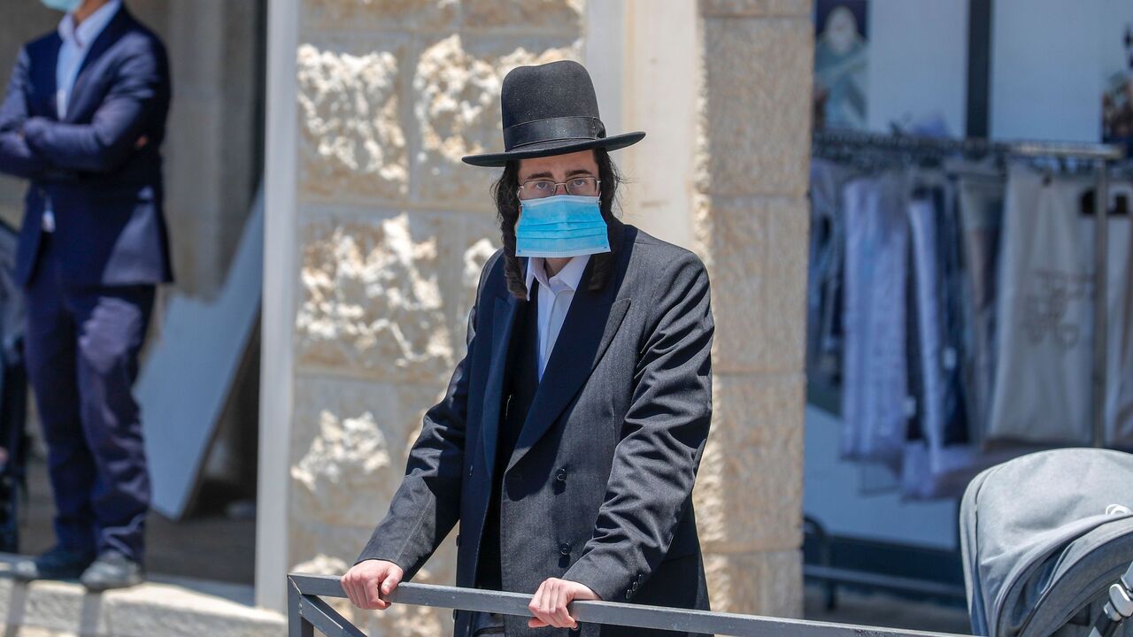 1226343854 An Ultra-Orthodox Jewish man, wearing a protective face mask, stands at a checkpoint erected to block entrance to the neighbourhoods of Romema and Kiryat Belz after authorities imposed a lockdown to combat the spread of the Coronavirus, in Jerusalem on July 12, 2020. (Photo by AHMAD GHARABLI / AFP) (Photo by AHMAD GHARABLI/AFP via Getty Images)