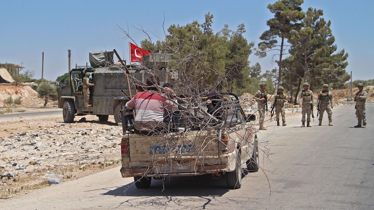 1227052369 Syrians sit in the back of a passing pick-up truck loaded with wood as Turkish soldiers deploy at the site of an improvised explosive device which hit a joint Turkish-Russian patrol on the strategic M4 highway, near the Syrian town of Ariha in the rebel-held northwestern Idlib province, on July 14, 2020. - Three Russian and several Turkish soldiers were wounded in Syria's restive Idlib province when a joint military patrol was hit by an improvised explosive device, Russia's defence ministry said. (Photo by