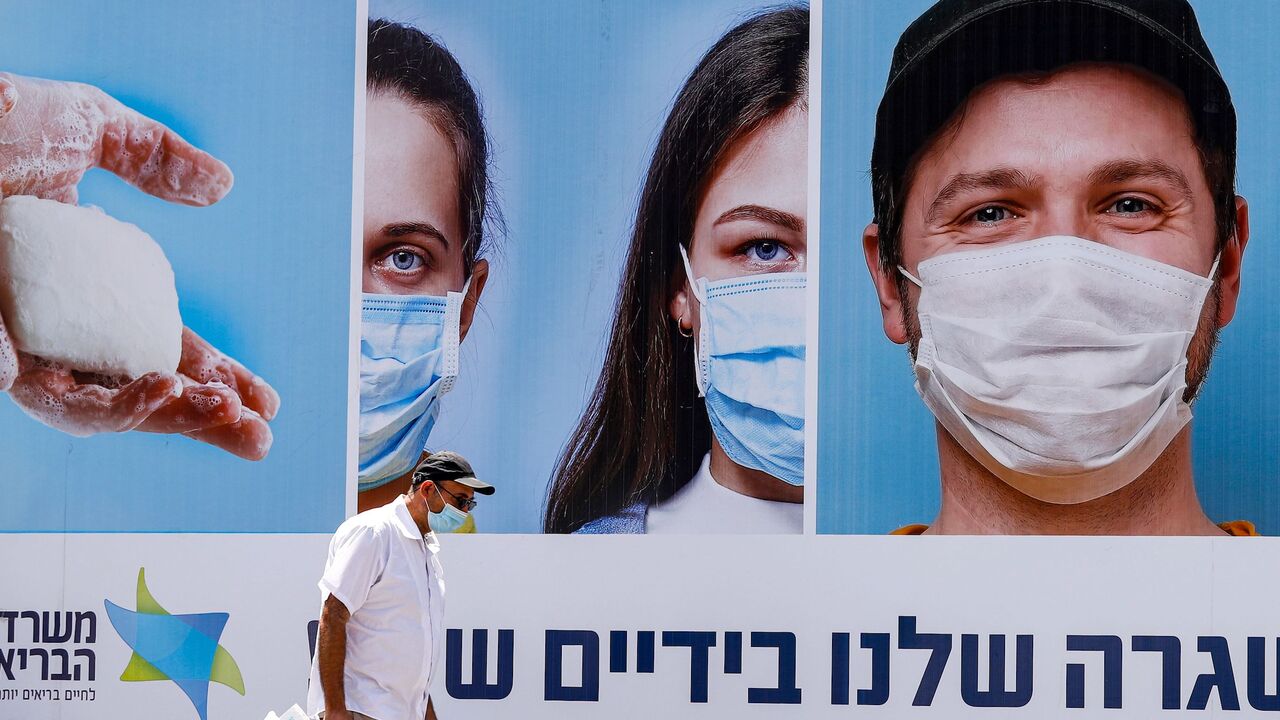 1227662855 A mask-clad man walks past a billboard showing other mask-clad faces and adequate social distance measures, raising awareness about COVID-19 coronavirus pandemic precautions, in the centre of the Israeli city of Ramat Gan, east of Tel Aviv, on July 17, 2020. - Israel's government said it was imposing new restrictions to limit the spiraling spread of coronavirus in the hope of avoiding a general lockdown further along the line. It said that from 5:00pm local time (1400 GMT) on Friday until 5:00am every Sunda