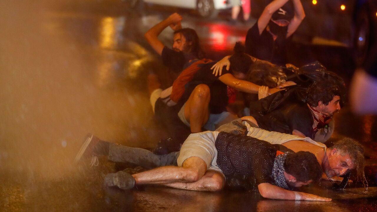 1227726885 TOPSHOT - Protesters crouch down as Israeli police use water cannons during clashes at a demonstration against the Israeli prime minister outside his official residence in Jerusalem, early on July 22, 2020. - Israeli Prime Minister Benjamin Netanyahu, 70, was indicted in January for bribery, fraud and breach of trust in three cases. He denies all the charges and accuses the media and legal officials of a witch hunt. (Photo by AHMAD GHARABLI / AFP) (Photo by AHMAD GHARABLI/AFP via Getty Images)