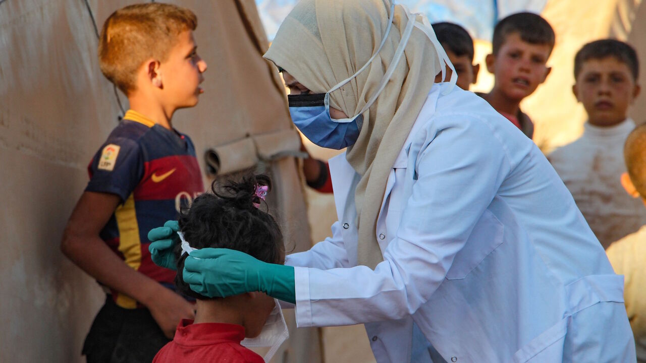 1227796416 A Syrian doctor, on her own initiative, instructs children how to properly wear a mask during the novel coronavirus pandemic crisis, in the displacement camp of Janid near the town of Dana, east of the Turkish-Syrian border in the northwestern Idlib province, on July 26, 2020. (Photo by Ibrahim YASOUF / AFP) (Photo by IBRAHIM YASOUF/AFP via Getty Images)