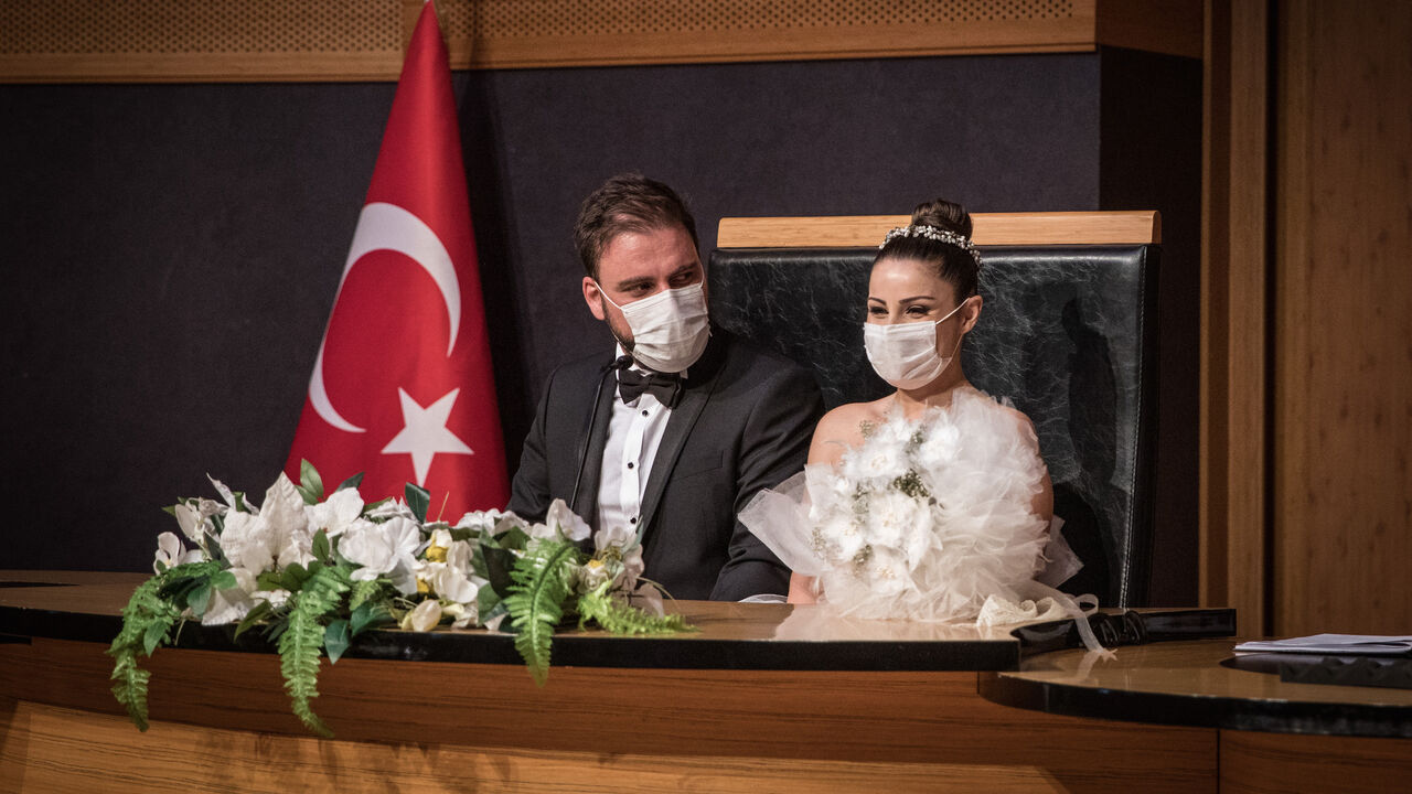 1253716043 ISTANBUL, TURKEY - JULY 01: Groom Okan Barut and bride Oya Kulaksiz wear face masks as they take part in their wedding ceremony at the Kadikoy Municipality marriage office on July 01, 2020 in Istanbul, Turkey. Restrictions on Turkish wedding halls were lifted on July 01, 2020 after being closed for months due to the Coronavirus pandemic. Turkey continues to slowly ease restrictions after recently reopening, cafes, restaurants, parks and inter-city travel. (Photo by Chris McGrath/Getty Images)