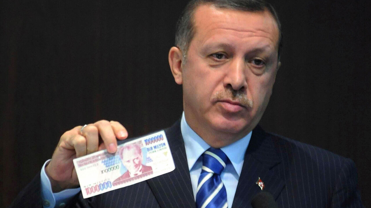 83099483 Turkish Prime Minister Tayyip Erdogan displays an banknote of the old Turkish Lira at a news conference in Ankara October 3, 2008. Turkey will return to its old currency, the Turkish Lira, on January 1, after a major money reform four years ago that saw the introduction of the New Turkish Lira. The banner in the background reads "The Turkish lira is coming". AFP PHOTO/ADEM ALTAN (Photo credit should read ADEM ALTAN/AFP via Getty Images)