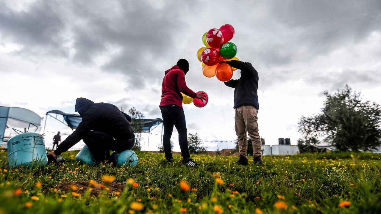 1199830173 Masked Palestinians prepare to attach balloons to a gas canister before releasing it near Gaza's Bureij refugee camp, along the Israel-Gaza border fence, on February 10, 2020. (Photo by MAHMUD HAMS / AFP) (Photo by MAHMUD HAMS/AFP via Getty Images)