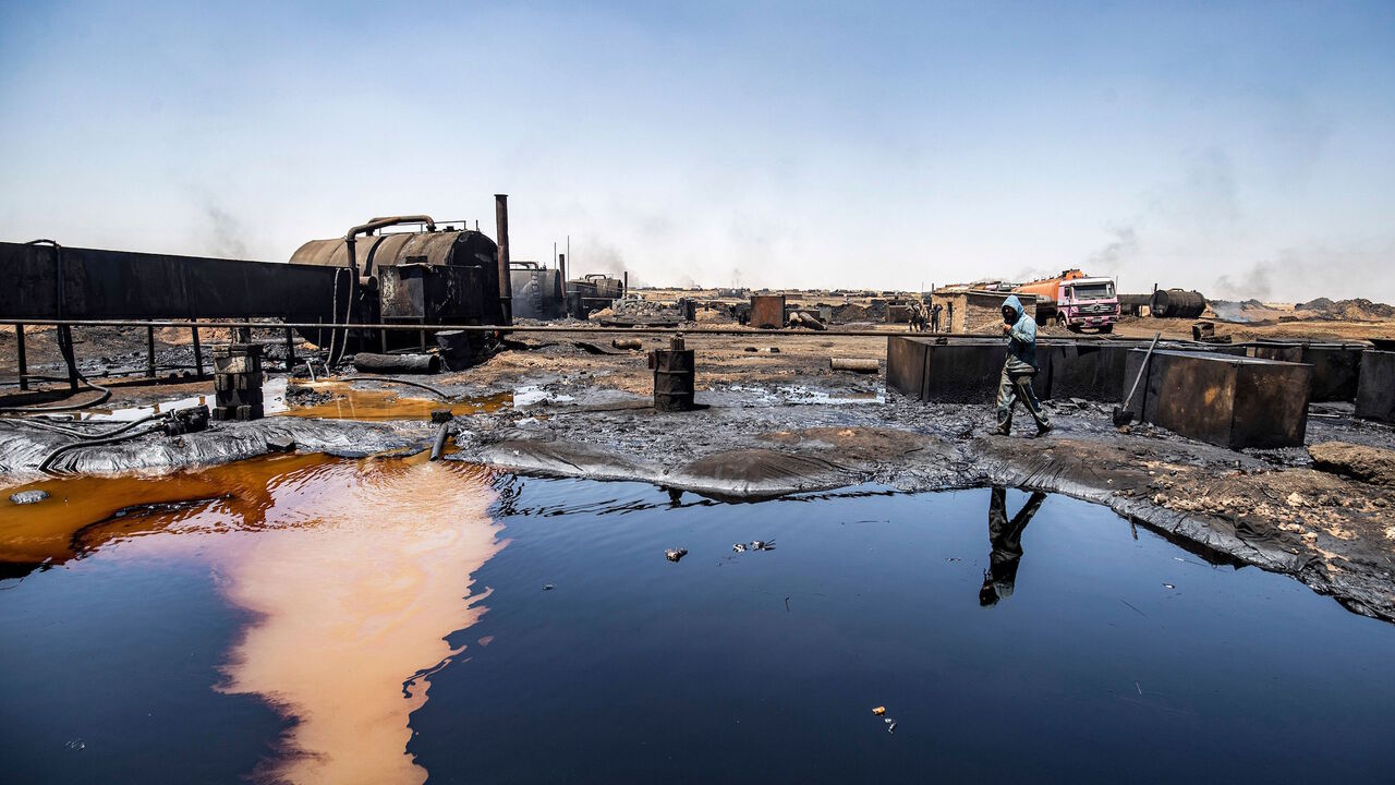 1227744016 A man walks at a makeshift refinery using burners to distill crude oil in the village of Bishiriya in the countryside near the town of Qahtaniya west of Rumaylan (Rmeilan) in Syria's Kurdish-controlled northeastern Hasakeh province, on July 19, 2020. - Oil pollution in Syria has become a growing concern since the 2011 onset of a civil war that has taken a toll on oil infrastructure and seen rival powers compete over control of key hydrocarbon fields. In the Kurdish-held northeast, a large storage facility i