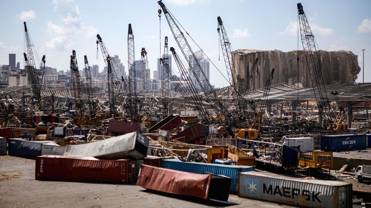 1227977720 This picture taken on August 9, 2020 shows a view of destroyed freight containers before the cranes at the port of Lebanon's capital Beirut, while in the background are seen the damaged grain silos opposite the blast site of a colossal explosion due to a huge pile of ammonium nitrate that had languished for years at a port warehouse. - The huge chemical explosion that hit Beirut's port, devastating large parts of the Lebanese capital and claiming over 150 lives, left a 43-metre (141 foot) deep crater, a sec