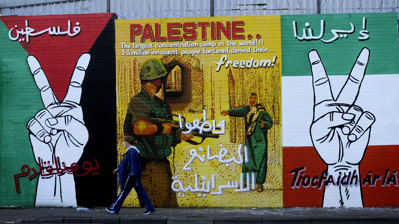 1345199 BELFAST, NORTHERN IRELAND - AUGUST 20: An unidentified girl walks past a portion of a mural on Falls Road August 20, 2002 in west Belfast, Northern Ireland. The pro-Palestinian painting has appeared in several Nationalist areas across Belfast in recent weeks. (Photo by Cathal McNaughton/Getty Images)