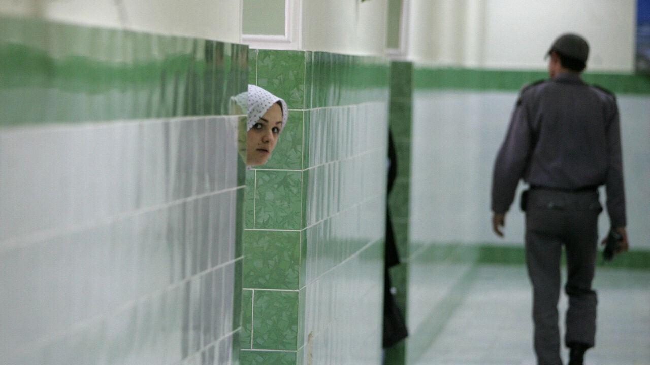 71193391 Tehran, IRAN: TO GO WITH AFP STORY IRAN-JUSTICE-PRISON-SOCIT BY PIERRE CELERIER An Iranian inmate peers from behind a wall as a guard walks by at the female section of the infamous Evin jail, north of Tehran, 13 June 2006. AFP PHOTO/ATTA KENARE (Photo credit should read ATTA KENARE/AFP via Getty Images)