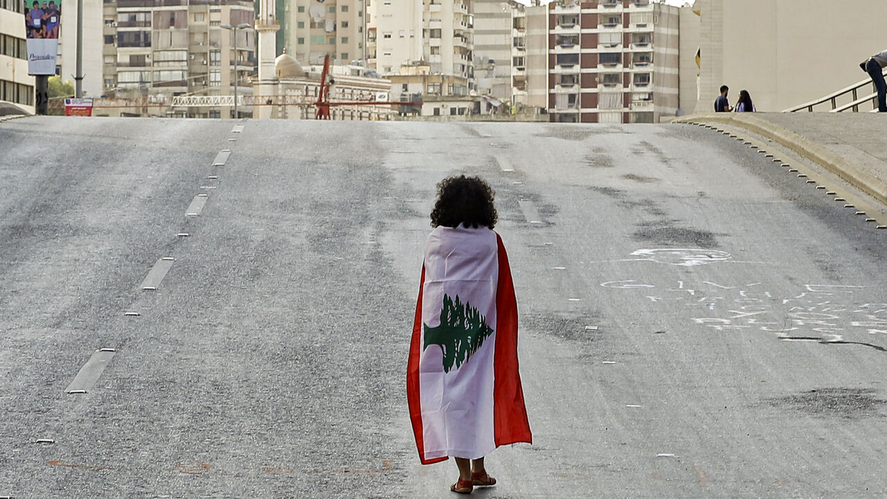 1178834680 TOPSHOT - A Lebanese woman protester walks draped in a national flag along the Fuad Chehab avenue, near the Martyrs' Square, in the centre of the capital Beirut on October 29, 2019 on the 13th day of anti-government protests. - An unprecedented cross-sectarian movement has brought major cities across Lebanon to a standstill since October 17, as protesters keep up demands for a complete overhaul of the political system. (Photo by JOSEPH EID / AFP) (Photo by JOSEPH EID/AFP via Getty Images)