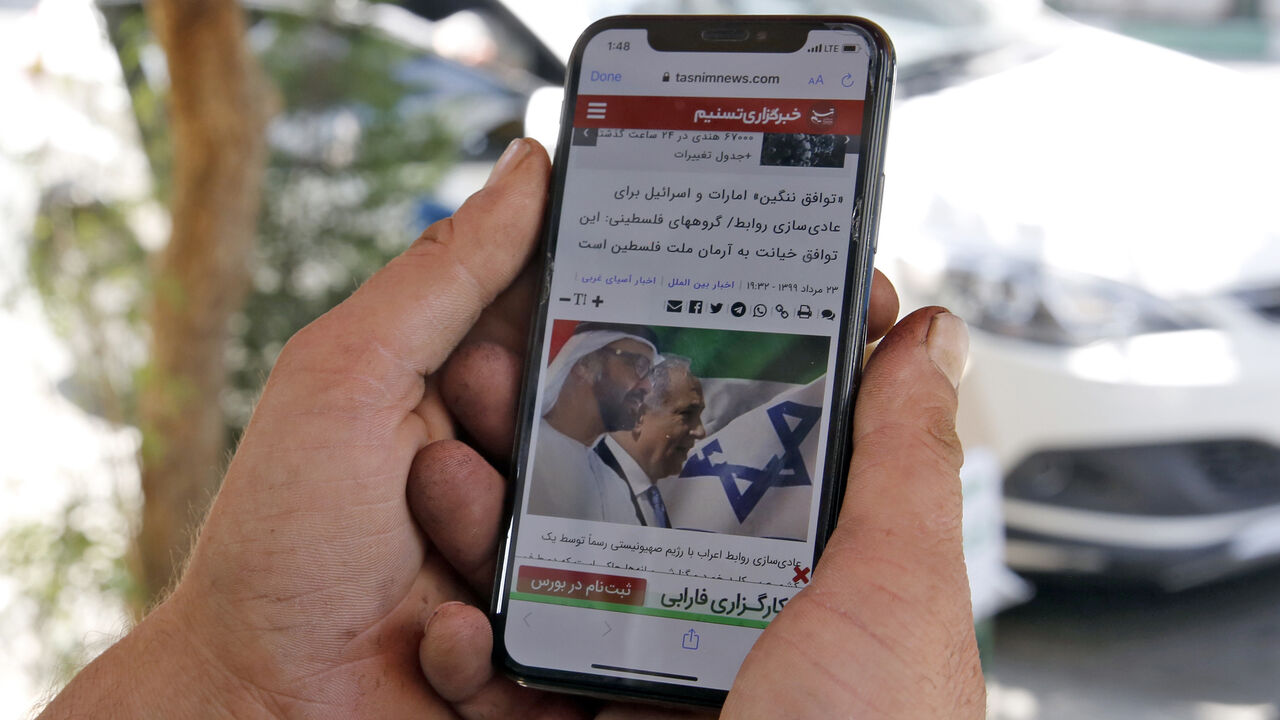1228038498 A man holds a phone while reading a story published on Tasnim News Agency's website about the recent news of a US-brokered deal between Israel and the UAE to normalise relations, in Iran's capital Tehran on August 14, 2020. - Iran strongly condemned the agreement, blasting it as an act of "strategic stupidity" that would only strengthen the Tehran-backed "axis of resistance". The Israel-UAE deal marks only the third such accord the Jewish state has struck with an Arab nation, an historic shift making the Gu