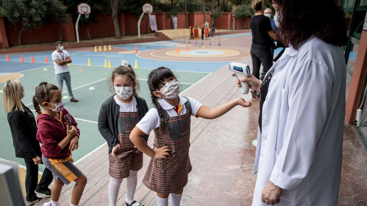 1273864612 ISTANBUL, TURKEY - SEPTEMBER 21: First grade students wearing protective face masks line up to have their temperature taken before entering the school building at the Florya Ugur College on September 21, 2020 in Istanbul, Turkey. For the first time since schools closed on March 16, due to the coronavirus outbreak, kindergarten and first grade students were allowed to return for in-person classes at schools across Turkey. The one day a week classes are voluntary and restarted amid strict coronavirus precauti
