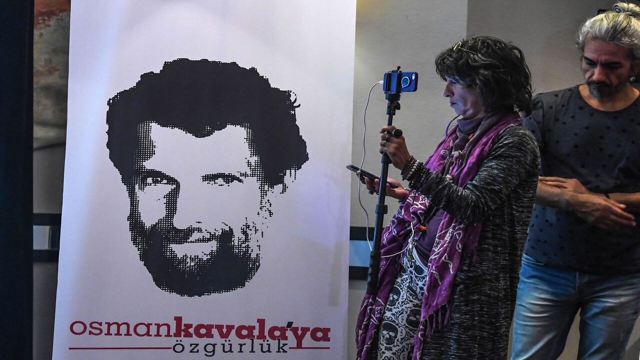 1055696742 A journalist stands in front of a poster featuring jailed businessman and philanthropist Osman Kavala during a press conference of his lawyers on October 31, 2018. - Osman Kavala was arrested a year ago by Turkish authorities and has still to be charged with an offence. (Photo by OZAN KOSE / AFP) (Photo credit should read OZAN KOSE/AFP via Getty Images)