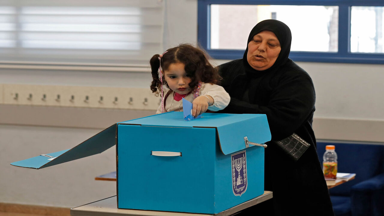 1204607270 An Arab Israeli woman holds a child casting her vote in a ballot box during the country's parliamentary elections at a polling station in the Arab city of Tamra in northern Israel on March 2, 2020. - Israelis were voting for a third time in 12 months today, with embattled Prime Minister Benjamin Netanyahu seeking to end the country's political crisis and save his career. (Photo by Ahmad GHARABLI / AFP) (Photo by AHMAD GHARABLI/AFP via Getty Images)