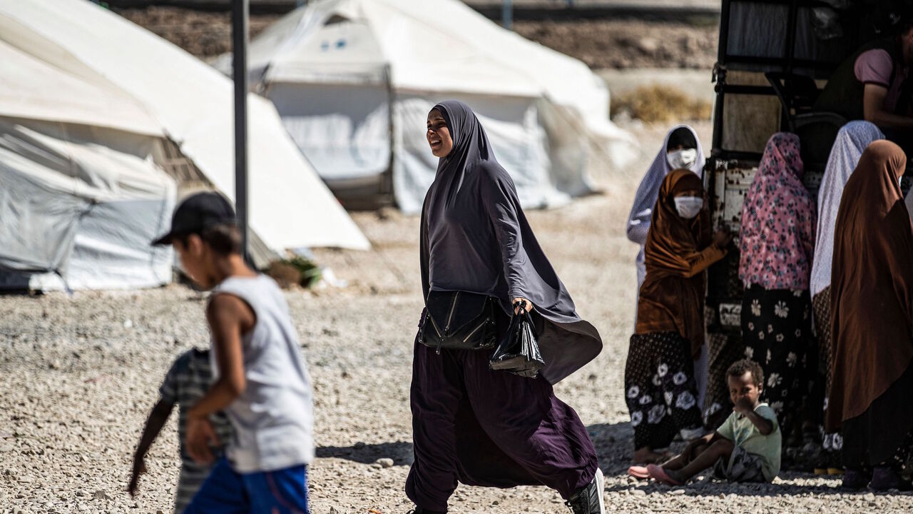 1228802096 A woman walks past others gathering by the back of a pickup truck at Camp Roj, housing family members of people accused to belong to the Islamic State (IS) group who were relocated from al-Hol camp, in the countryside near al-Malikiyah (Derik) in Syria's northeastern Hasakah province on September 30, 2020. (Photo by Delil SOULEIMAN / AFP) (Photo by DELIL SOULEIMAN/AFP via Getty Images)