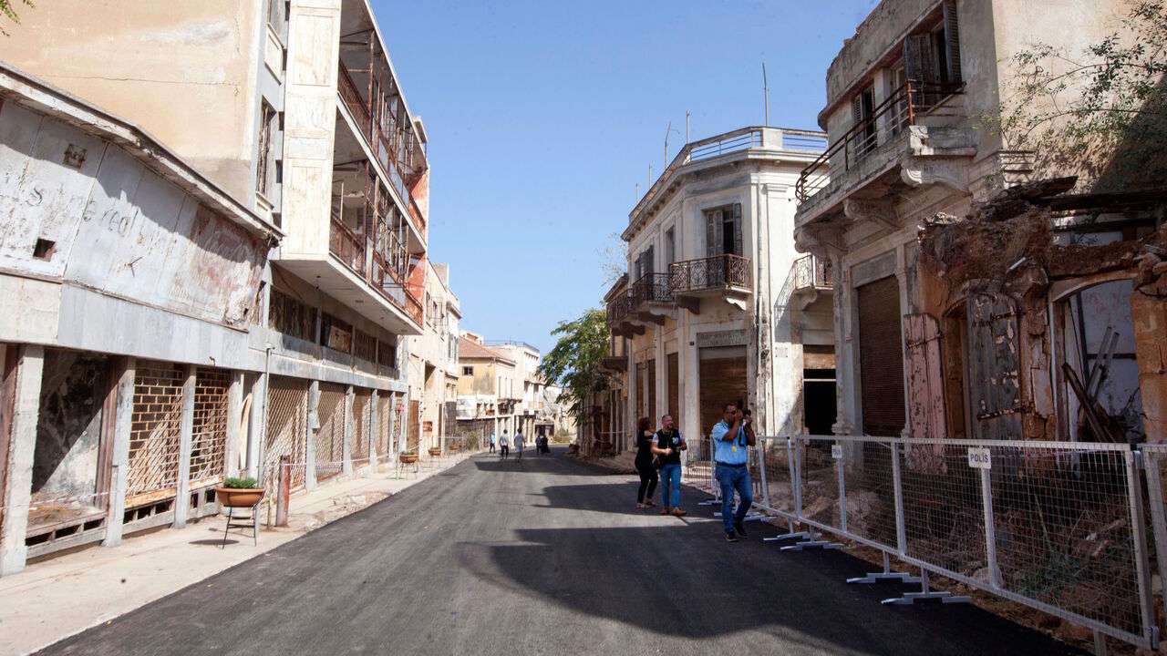 1228961007 Journalists film as they walk past abandoned buildings along a street in Varosha, in the fenced off area of Famagusta, in the Turkish-occupied north of the divided eastern Mediterranean island of Cyprus. - Turkish troops partially reopened the Cyprus seaside resort of Varosha, sealed off since its Greek Cypriot inhabitants fled in 1974, sparking controversy days before a Turkish Cypriot election. (Photo by Birol BEBEK / AFP) (Photo by BIROL BEBEK/AFP via Getty Images)
