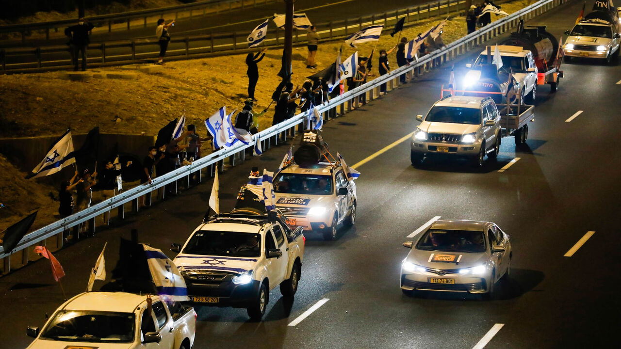 1229068945 Drivers on the highway leading to Jerusalem wave Israeli national flags as they protest against the prime minister and against the second nationwide lockdown imposed by the government in a bid to stem the increase of COVID-19 infection cases, at the entrance of Jerusalem on October 14, 2020. (Photo by Ahmad GHARABLI / AFP) (Photo by AHMAD GHARABLI/AFP via Getty Images)