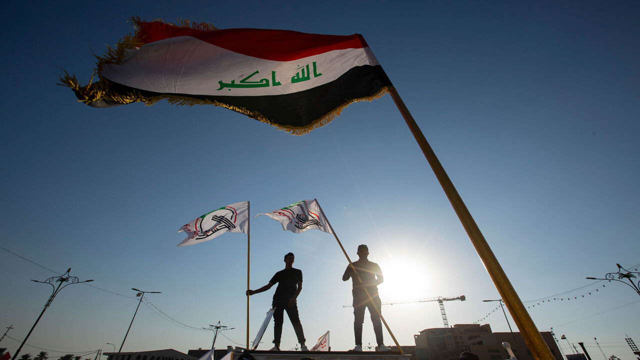 1229125266 Supporters of Hashed al-Shaabi, an Iraqi paramilitary network dominated by Iran-backed factions, wave the Hashed flag as they stand under the national flag during a protest denouncing comments made by Kurdish ex-minister and to show their support to the paramilitary network in the southern Iraqi city of Basra on October 17, 2020. - Hashed supporters burned down the main Kurdish party's headquarters in Baghdad after criticism from a Iraq's Former Foreign Minister Hoshyar Zebari. Hundreds of Hashed demonstrat