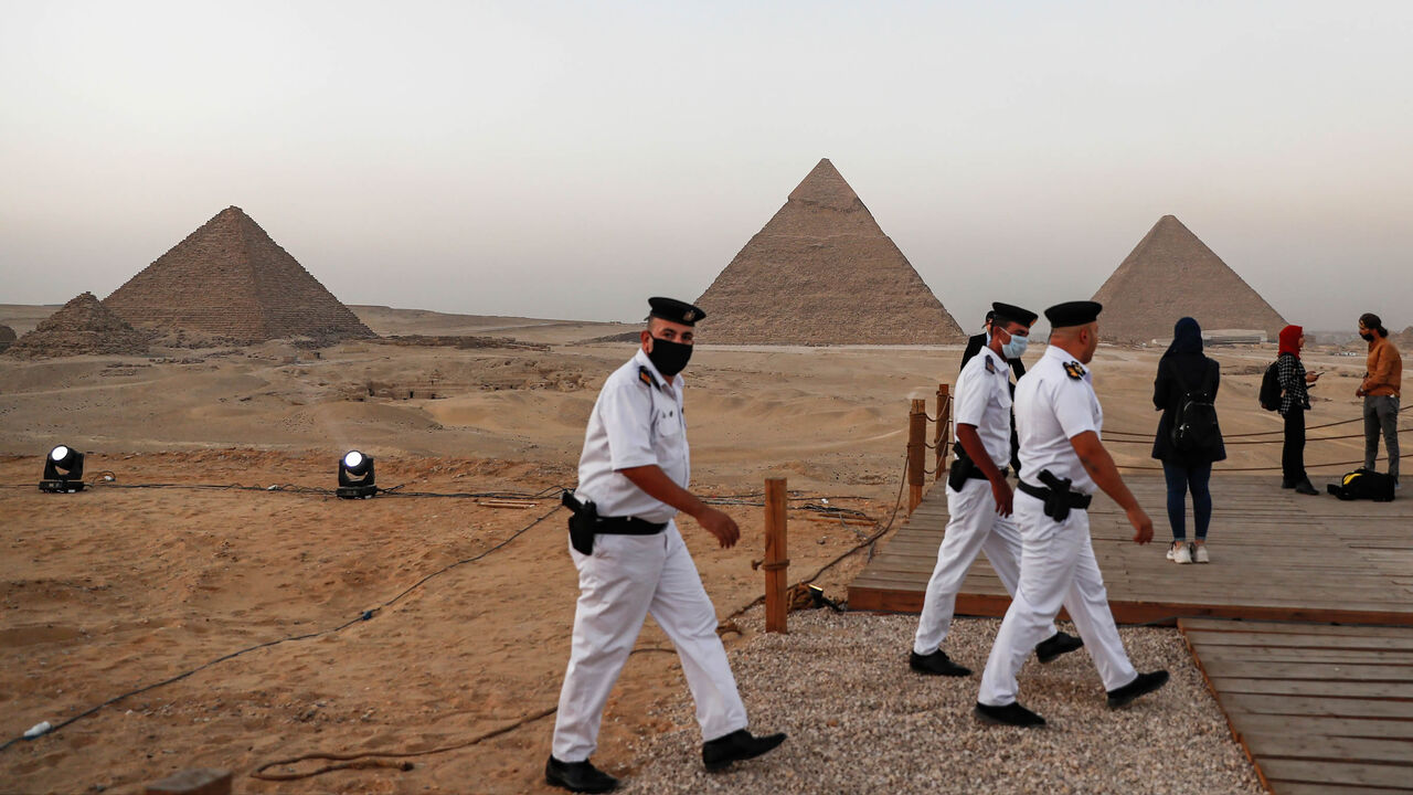 1229193325 Policemen walk along a promontory overlooking (R to L) the Great Pyramid of Khufu (Cheops), the Pyramid of Khafre (Chephren), and the Pyramid of Menkaure (Menkheres) at the Giza Pyramids necropolis on the southwestern outskirts of the Egyptian capital Cairo on October 20, 2020 before an official ceremony launching the trial operations of the site's first environmentally-friendly electric bus and restaurant as part of a wider development plan at the necropolis. (Photo by Khaled DESOUKI / AFP) (Photo by KHALE
