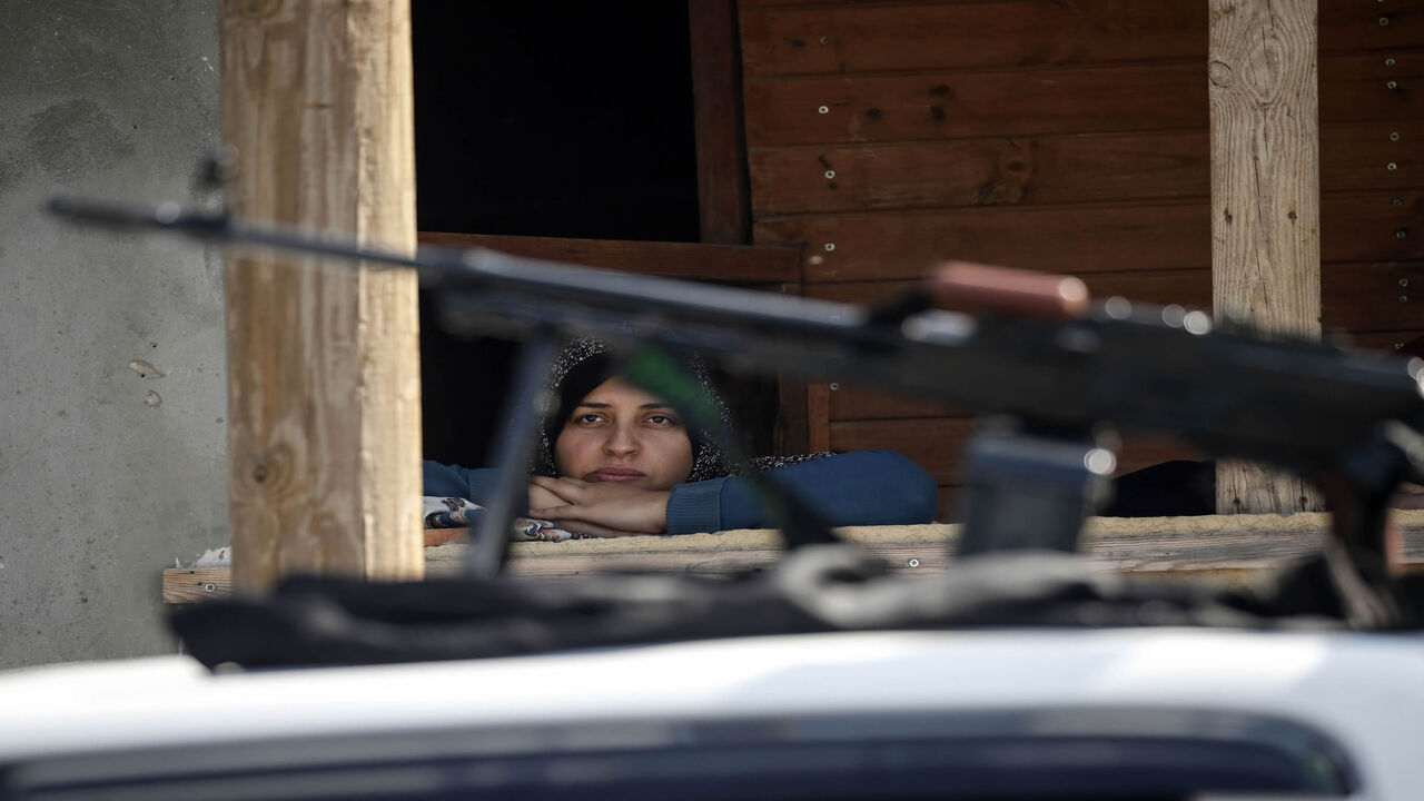 1181679088 A Palestinian woman watches from her home's window fighters from the Ezz-Al Din Al-Qassam Brigades, the armed wing of the Hamas movement, taking part in an anti-Israel military show in Khan Yunis in the southern Gaza Strip November 11, 2019 to mark one year since their comrade Nour Baraka, a commander in the group, was killed in an Israeli military operation in the Gaza Strip. (Photo by SAID KHATIB / AFP) (Photo by SAID KHATIB/AFP via Getty Images)