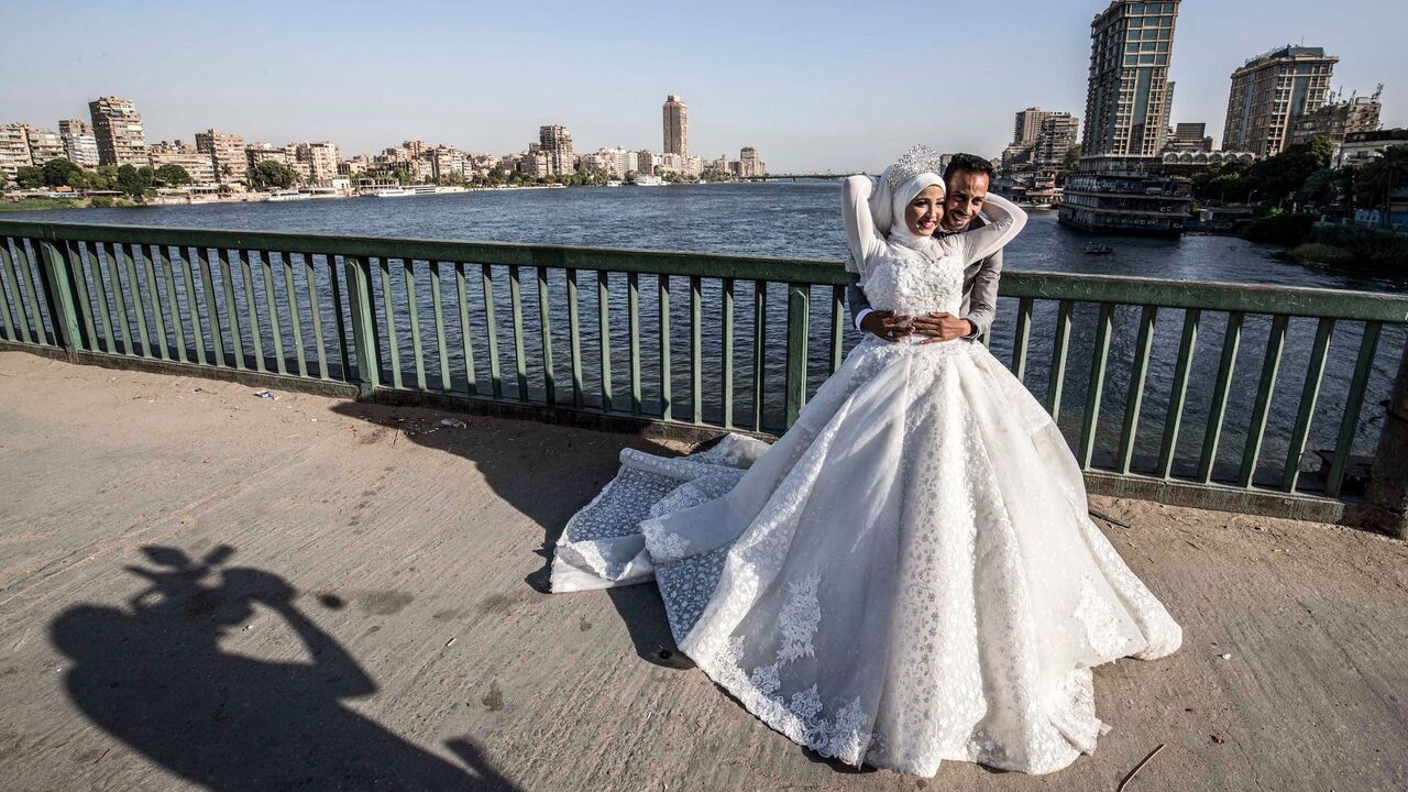 1219321254 Ragab Uwais, 29, poses for a picture with his bride before a video cameraman for their wedding video along al-Gamaa bridge connecting the Egyptian capital Cairo with its twin city of Giza, on June 11, 2020. (Photo by Khaled DESOUKI / AFP) (Photo by KHALED DESOUKI/AFP via Getty Images)