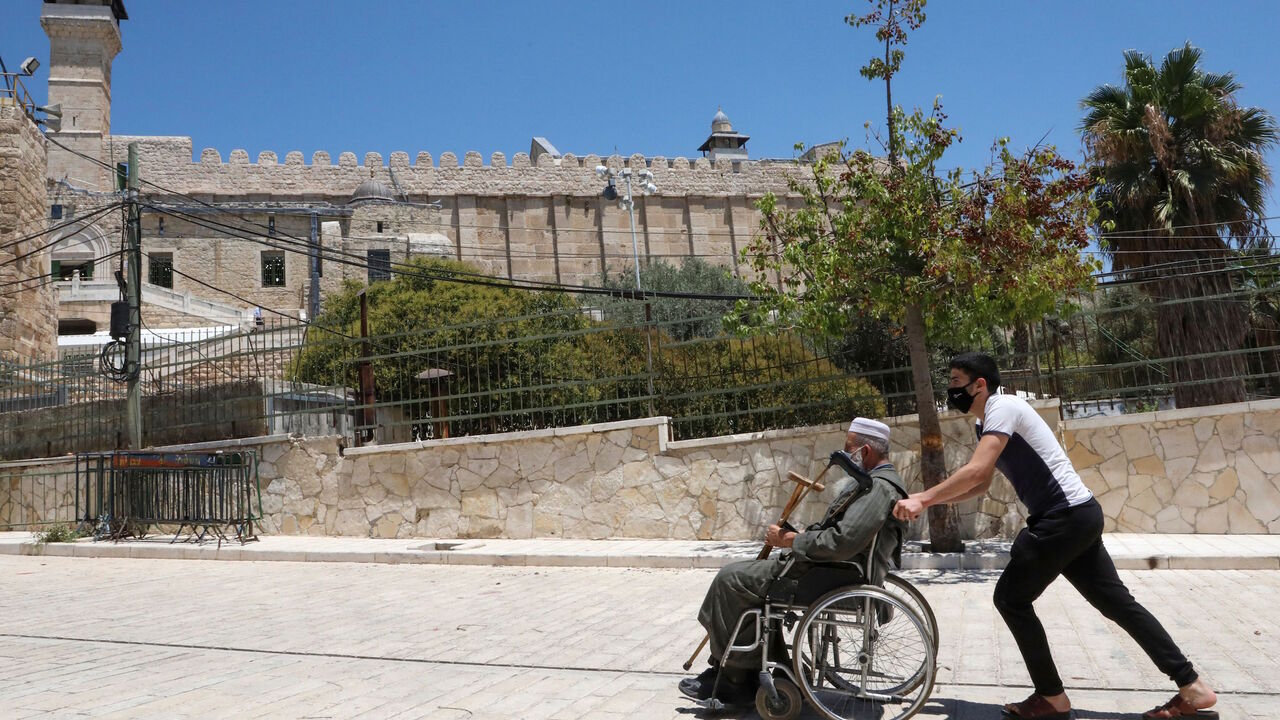 1227948837 A Palestinian youth pushes an elderly man next to the Ibrahimi mosque (background), also known as the Tomb of the Patriarchs, in the occupied West Bank city of Hebron on August 7, 2020, amid the ongoing coronavirus pandemic crisis. (Photo by HAZEM BADER / AFP) (Photo by HAZEM BADER/AFP via Getty Images)