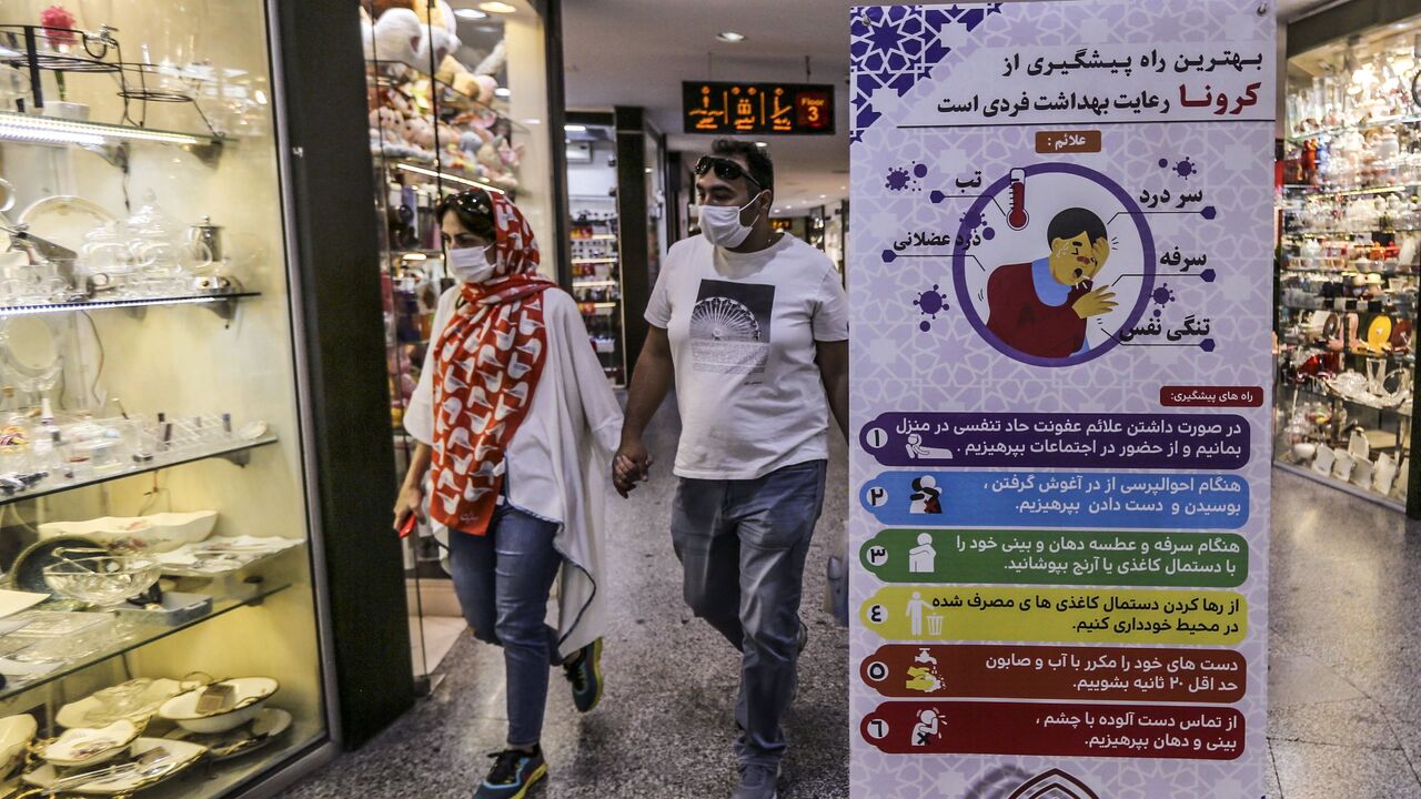 1229392947 Iranians walk next to a sign advising people to wear masks as they shop in Tajrish square in the capital Tehran on November 1, 2020, amid the novel coronavirus pandemic crisis. - Iran yesterday announced the expansion beyond Tehran of measures against Covid-19, amid growing calls for a full lockdown after the country posted a string of record highs in deaths and infections. (Photo by ATTA KENARE / AFP) (Photo by ATTA KENARE/AFP via Getty Images)