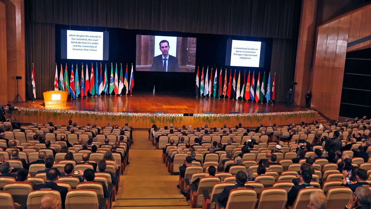 1229574527 Syria's President Bashar al-Assad (on screen) addresses via video link the opening session of the international conference on the return of refugees held in Damascus on November 11, 2020. - Syria's government kicked off a two-day Russia-backed conference in Damascus towards facilitating the return of millions of Syrian refugees to the war-torn country, despite reservations within the international community. (Photo by LOUAI BESHARA / AFP) (Photo by LOUAI BESHARA/AFP via Getty Images)